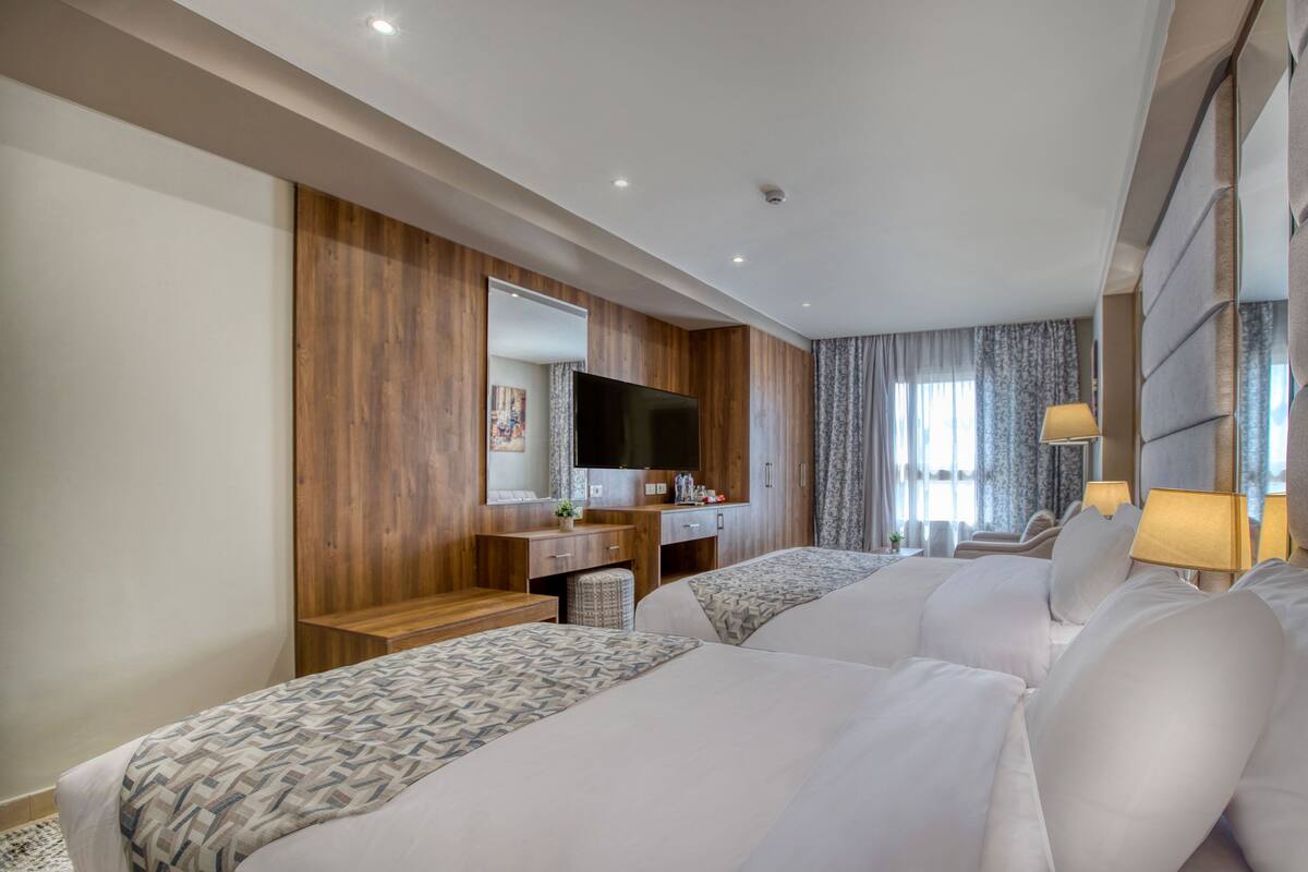A hotel room with two beds, a wooden dresser, a flat-screen TV, and a desk with a lamp.
