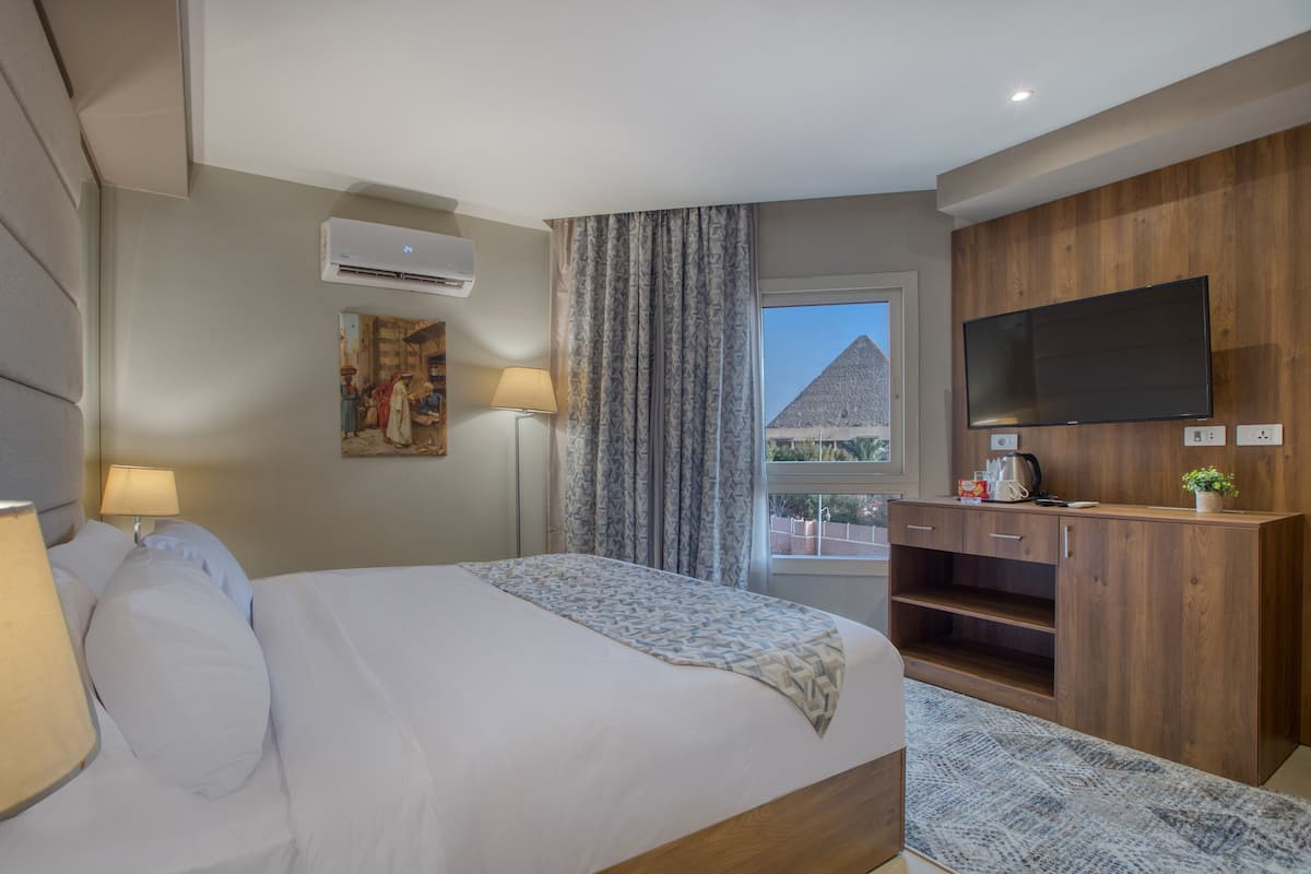 A modern hotel room with a bed, a flat-screen TV, a wooden cabinet, and a window with a view of a pyramid.