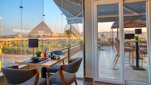 Un comedor con mesa y sillas, un ventilador y vistas a una pirámide a lo lejos.