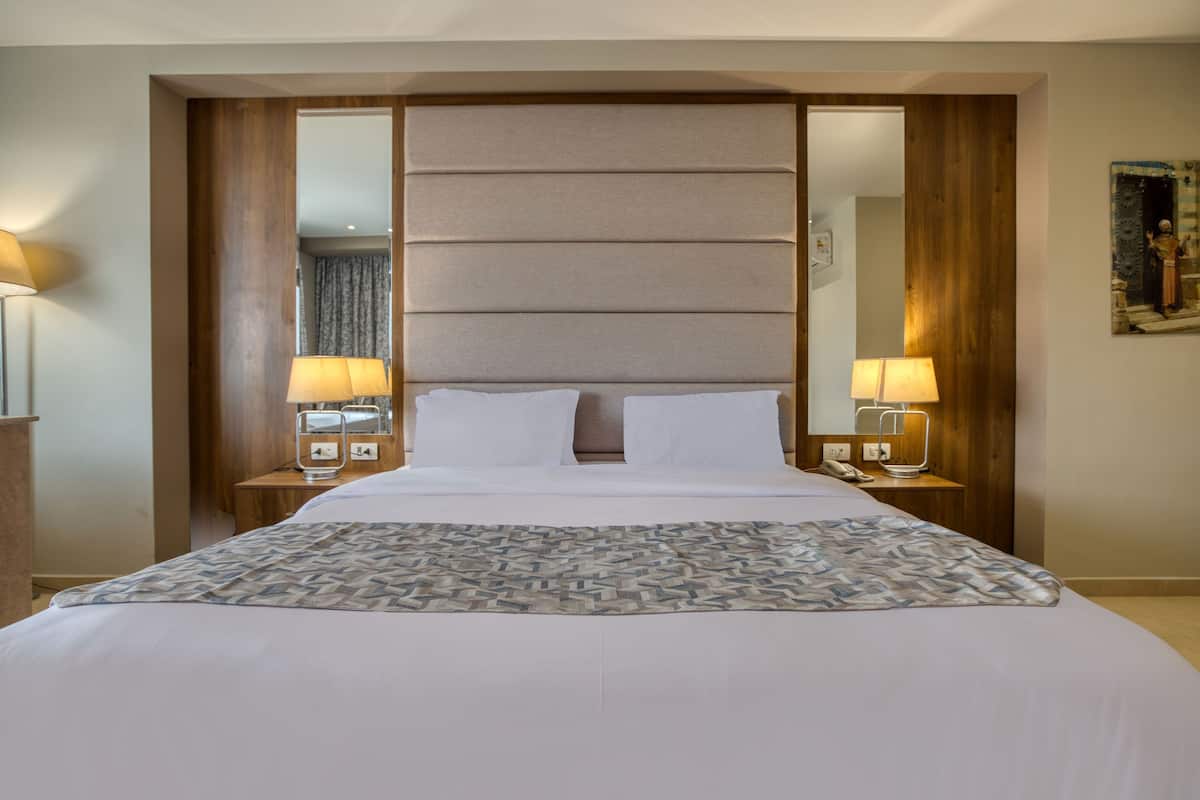 A hotel room with a large bed, two bedside tables with lamps, a headboard, and a mirror.