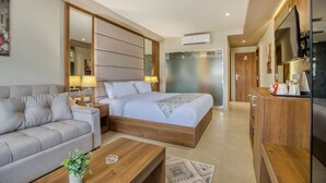 Una habitación de hotel moderna con cama, sofá, mesitas de noche, televisor y minibar.