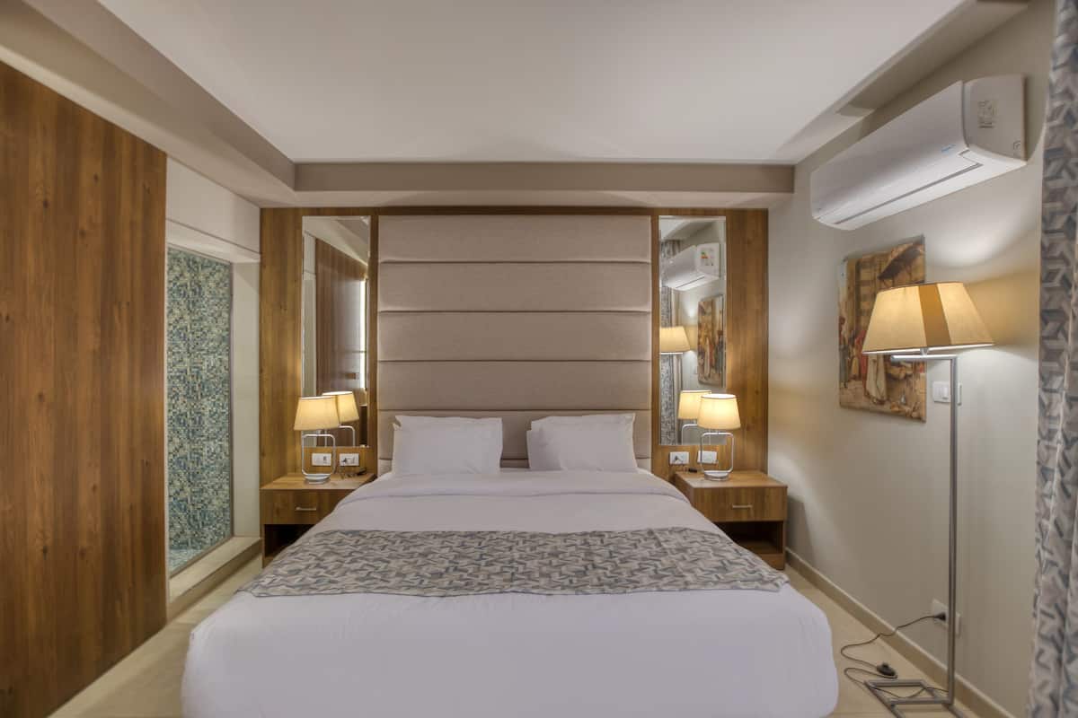 A hotel room with a large bed, wooden paneling, a mirror, two bedside lamps, and an air conditioning unit.