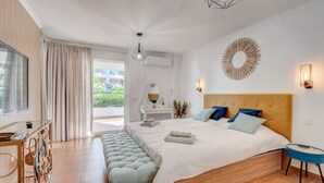 Quarto moderno com uma cama grande, um banco, cômoda e vista para o exterior.