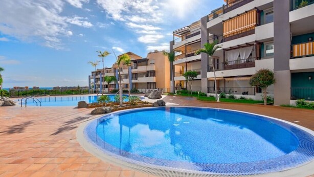 Um hotel moderno com uma piscina grande, várias varandas e vista clara para o mar.