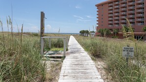 Une promenade en bois mène à une plage, et un panneau indique qu’il est interdit de marcher sur les dunes.