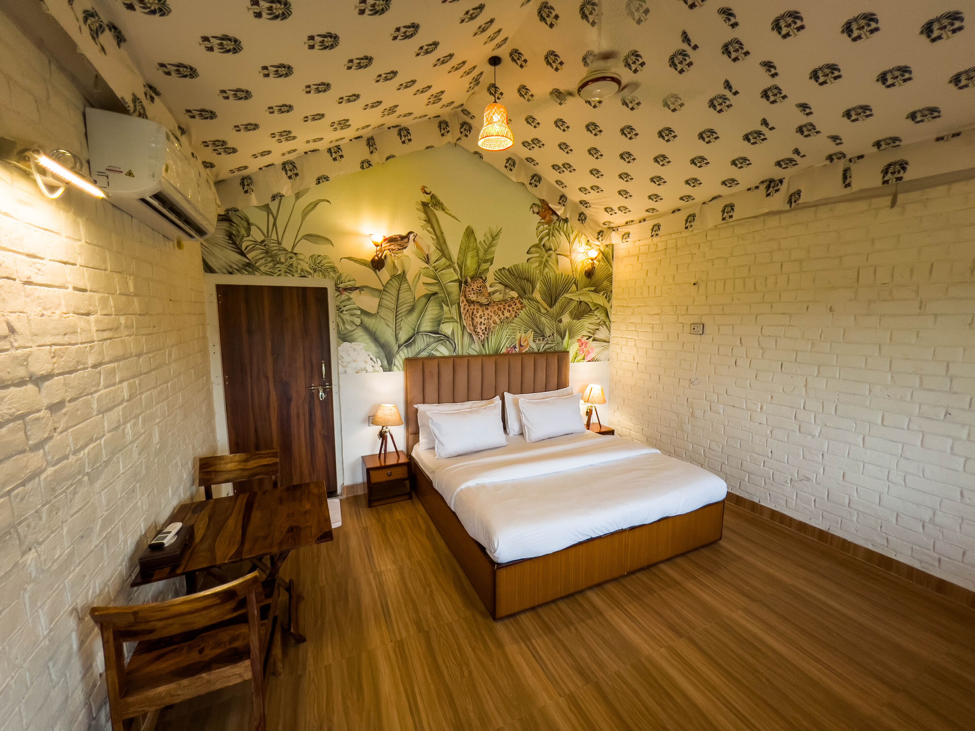 A bedroom with a wooden bed, a desk, and a chair. There is a brick wall and a ceiling with a pattern.