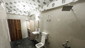 A bathroom with a toilet, sink, and shower. The floor is black marble, and the walls are white with a pattern. There is a wooden door and a mirror on the wall. - Vanbagh Sariska Resort (Alwar)