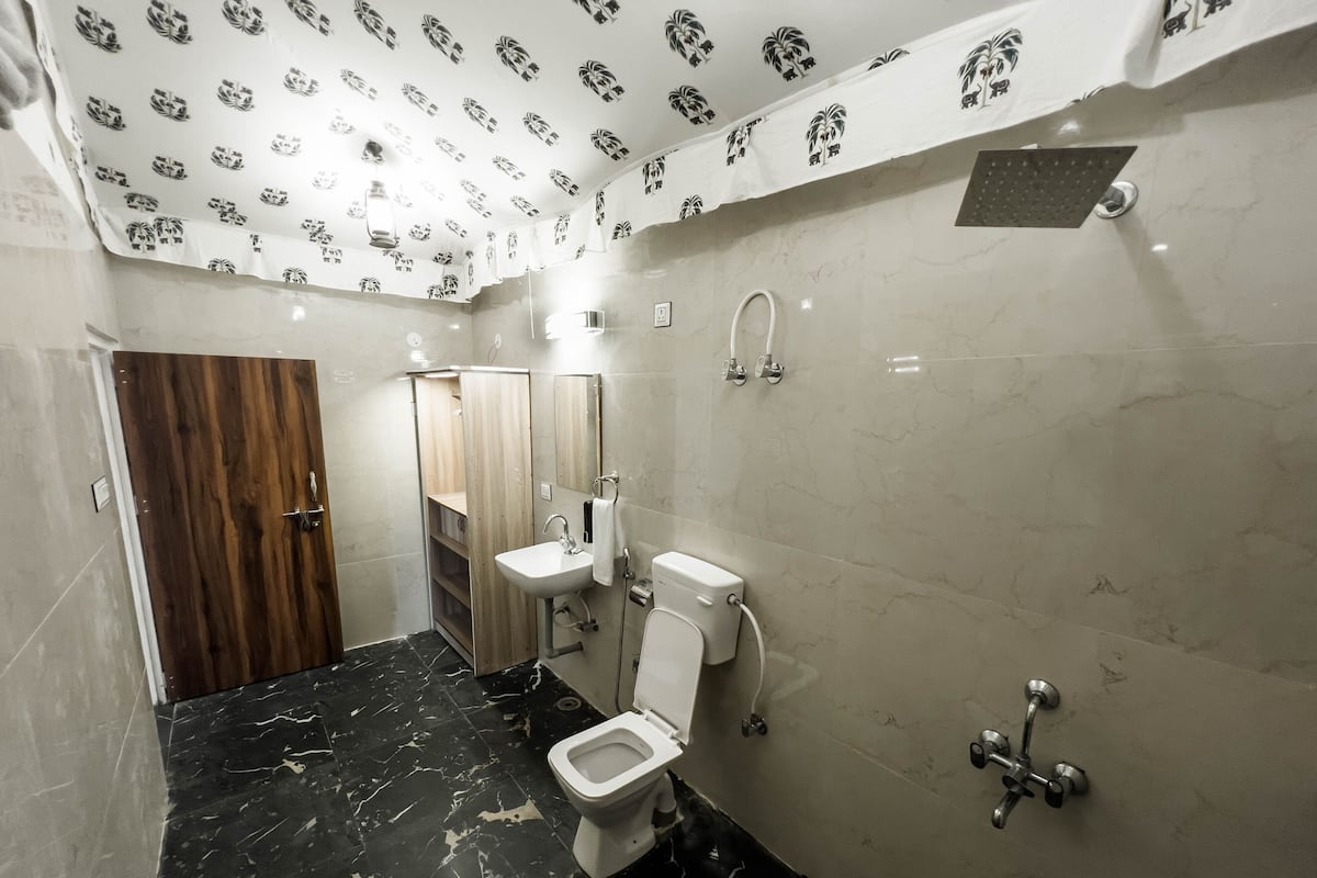 A bathroom with a toilet, sink, and shower. The floor is black marble, and the walls are white with a pattern. There is a wooden door and a mirror on the wall.