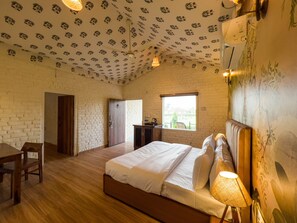 Ein Schlafzimmer mit Holzboden, einem Bett mit weißen Leinen, einem Schreibtisch und einem Stuhl. Ein Fenster bietet einen Ausblick nach draußen.