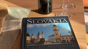 A bottle of Matysak wine and a book titled "Slovakia: Historic Architecture Creative Art Sights" on a wooden table.