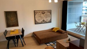 A modern living room with a brown sofa, a dining table with chairs, a globe artwork, and a large window with a view of the outside.
