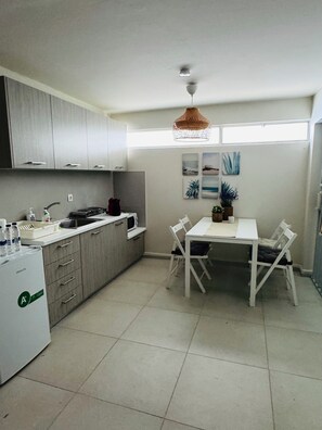 A modern kitchen with grey cabinets, a white countertop, a dining table with chairs, and a ceiling fan.