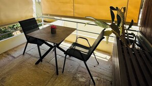 Un'area esterna coperta con posti a sedere, un tavolo, sedie, una pianta in vaso e vista sulla strada.