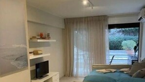 Una camera da letto moderna con un letto, una TV su un mobile, un balcone con una sedia e una finestra con tende.