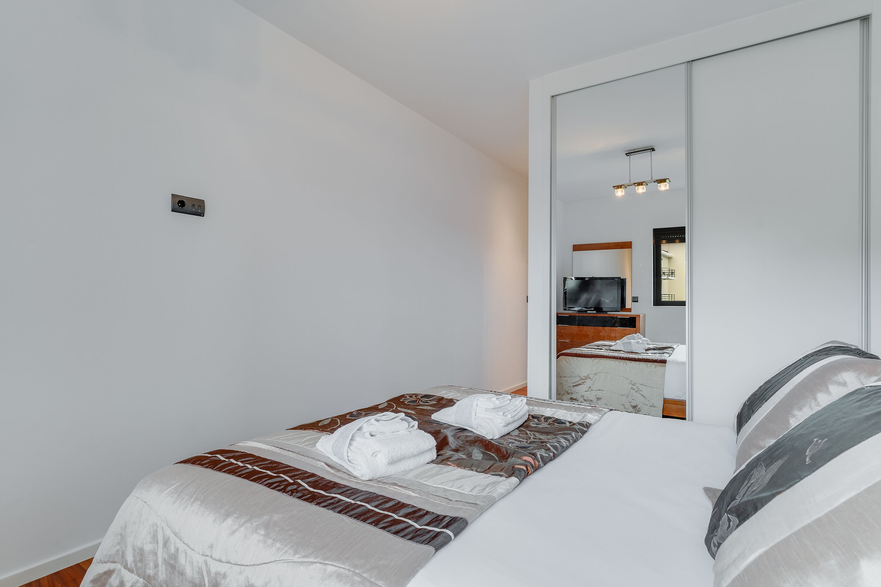 A modern hotel room with a large bed, a mirror, and a television.