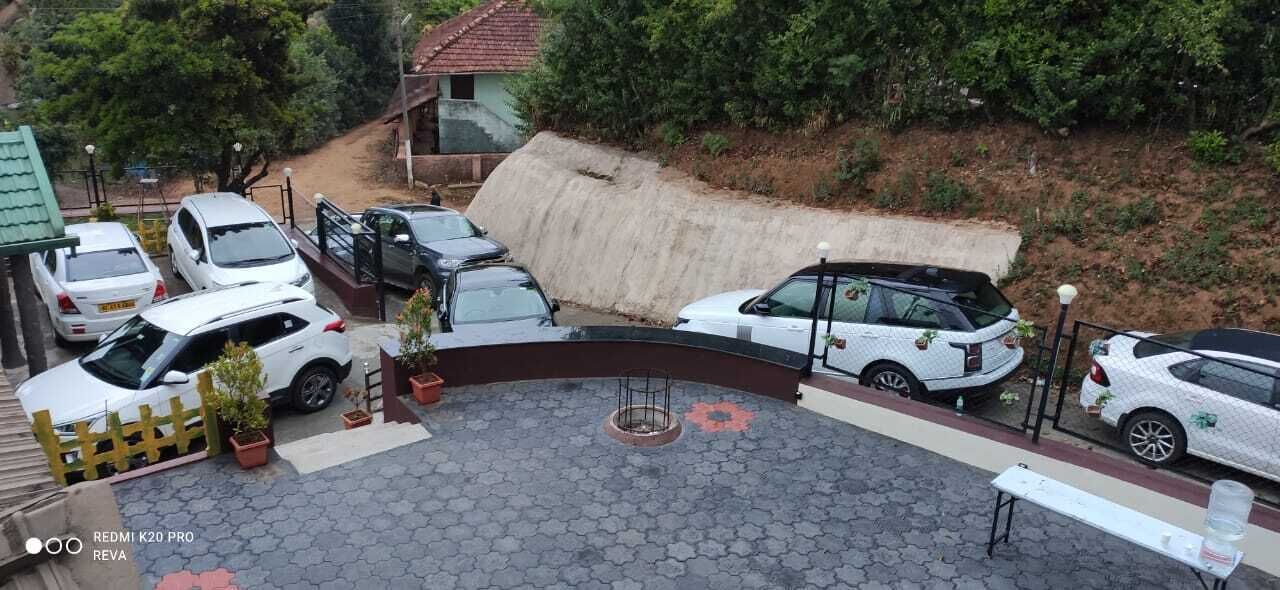 Un área de estacionamiento con varios coches blancos, una barrera de hormigón y un pequeño edificio con techo rojo.
