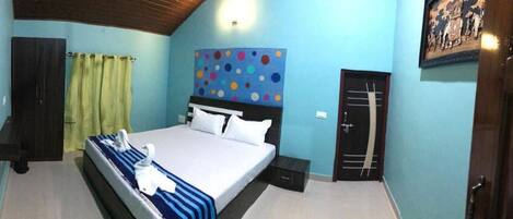 A bedroom with a bed, a headboard with a colorful pattern, a wardrobe, a door, and a wall-mounted light fixture.