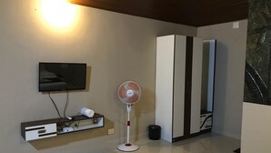 Une chambre moderne dotée d’un téléviseur à écran plat fixé au mur, d’un ventilateur sur pied, d’une armoire et d’un sol qui ressemble à du marbre.