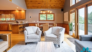 Een ruime woonkamer met houten plafond, een eettafel met stoelen, en een groot raam met uitzicht op de omgeving.