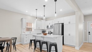 Une cuisine moderne avec des meubles blancs, un îlot central doté de tabourets, des appareils en acier inoxydable et un éclairage suspendu.