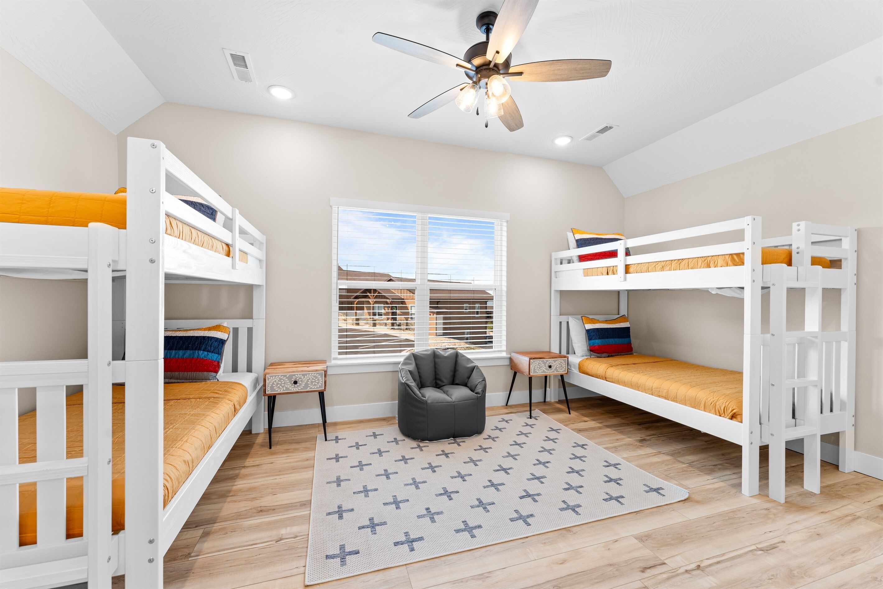 A room with bunk beds, a ceiling fan, a window, and a bean bag chair.
