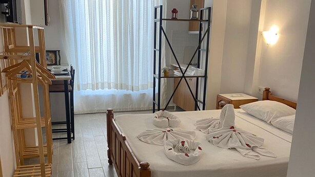 Habitació d'hotel amb llit de fusta, escriptori, cadira, armari i finestra amb cortines.