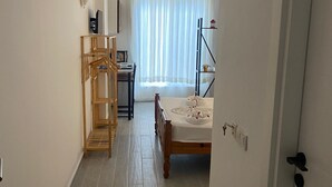 Passadís estret que condueix a una habitació amb un llit, un armari de fusta i un escriptori amb cadira.