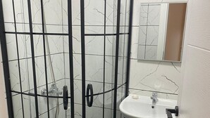 Un bany amb dutxa de vidre, un lavabo de pedestal i un vàter.
