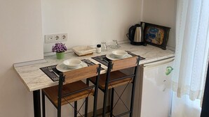 Una cuina senzilla amb armaris de fusta, taulell de marbre i un refrigerador petit.