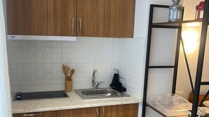 Cuina amb armaris de fusta, taulell blanc, rentapelats i prestatge metàl·lic amb un llum lluminosa.
