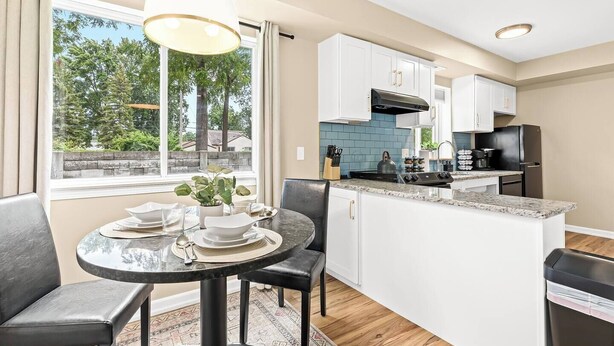 A modern kitchen with white cabinets, a black refrigerator, and a dining area with a round table and chairs.