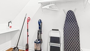 A neatly organized laundry area with a steam iron, a vacuum cleaner, a mop, and a ladder.