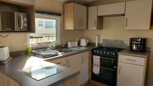 A compact kitchen with a gas stove, oven, and a coffee maker. - 2 Brightholme 6 Berth With Decking & Enclosed Gard (Burnham-on-Sea)
