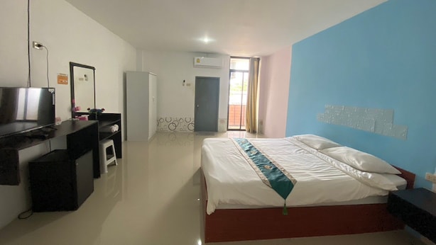 A hotel room with a bed, a desk with a computer, a wardrobe, and a door leading to a balcony. - Ruen Bua resident (Warin Chamrap)