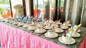A table set with white cups and saucers, each containing a spoon and a packet of snacks. - Ruen Bua resident (Warin Chamrap)