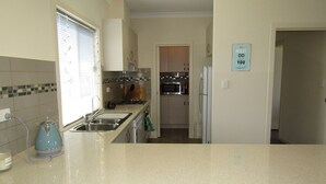 Una cocina compacta con lavamanos, estufa, microondas y refrigerador. Se observa un cartel de 'No molestar' en la pared.