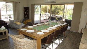 Un comedor con una larga mesa de madera dispuesta para seis personas, rodeada de sillas de mimbre.
