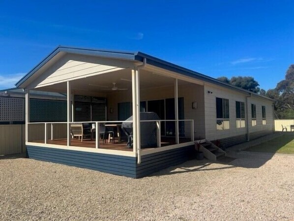 A single-story mobile home with a covered porch, a small patio area, and a fenced yard.