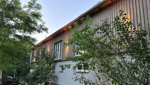 Rakennus, jonka ulkoseinät ovat puuta ja jossa on useita ikkunoita. Sen ympärillä on vehreää kasvillisuutta ja nurmikko.