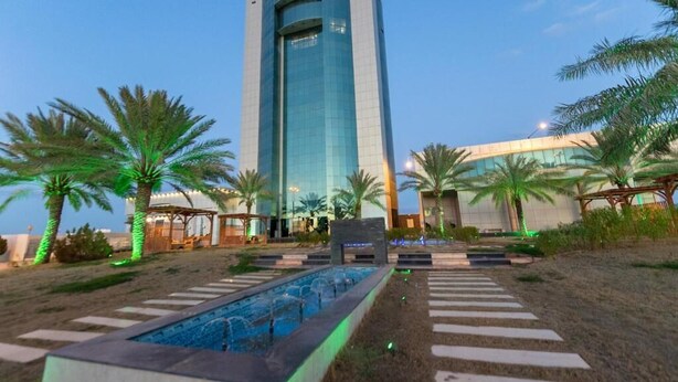 A modern hotel with a tall, curved glass facade, a swimming pool, and palm trees.