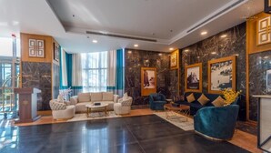 A spacious lobby with a black marble floor, a beige sofa set, a blue velvet armchair, and framed pictures on the walls.