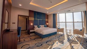 A hotel room with a large bed, two armchairs, a desk, and a view of the city.
