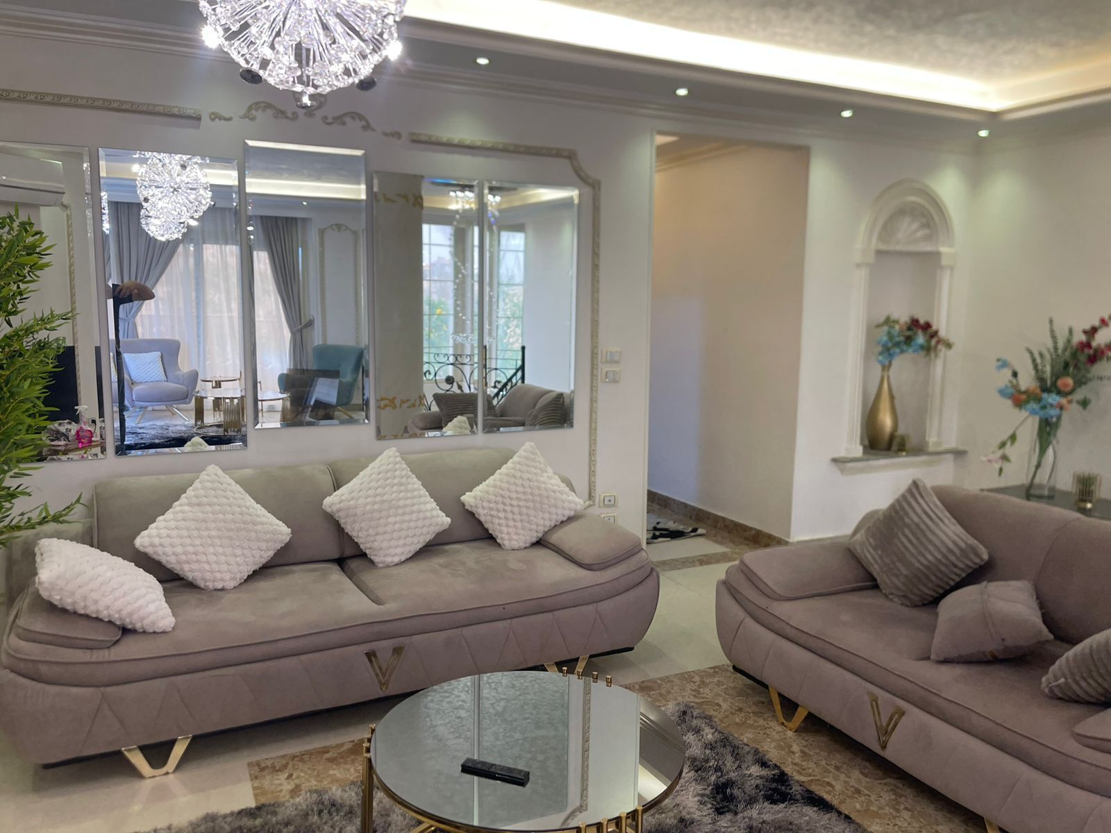 A modern living room with two sofas, a glass coffee table, and a chandelier.
