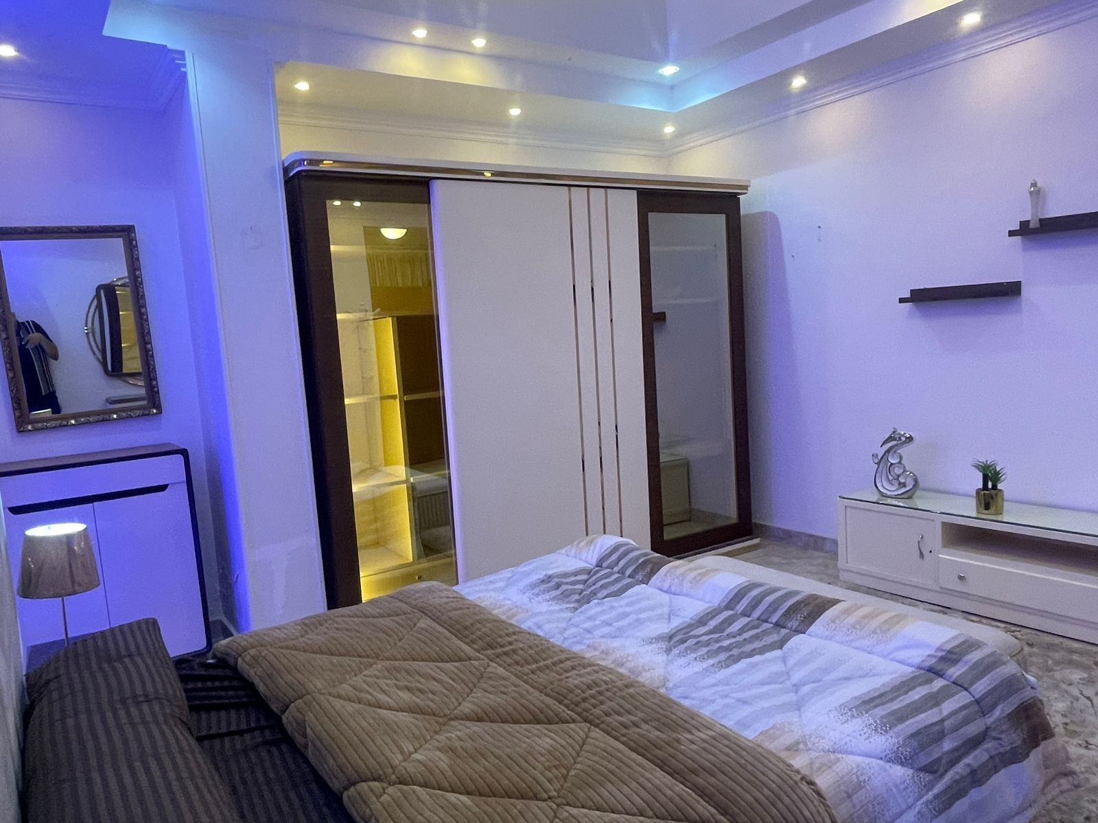 Een slaapkamer met een bed, een kledingkast, een spiegel en een bedlamp.