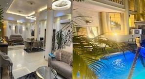 A luxurious living room with a dining area, a staircase with ornate railings, and a pool area with palm trees.