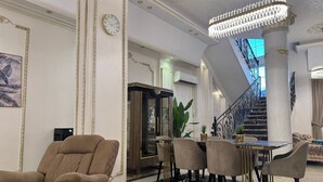 Een ruime woonkamer met een hoge plafond, een kroonluchter, een trap en een eethoek met stoelen en een tafel.
