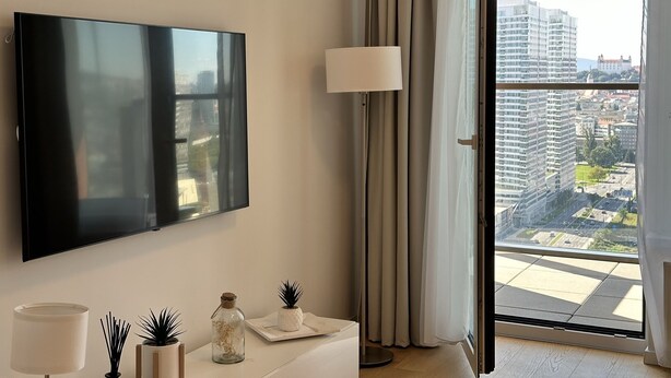 Een moderne woonkamer met een flatscreen televisie, een lamp en een klein tafeltje met decoratieve objecten.