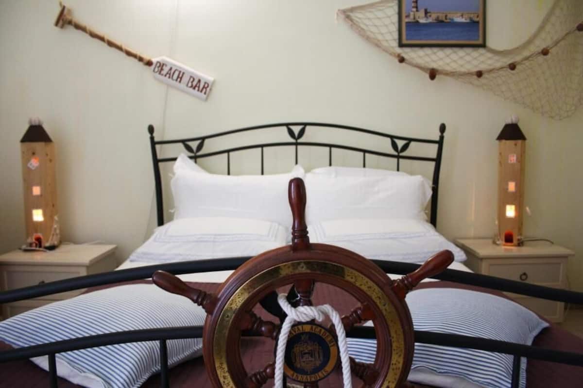 Ein Bett mit Kopfstütze in Form eines Schiffsrades, zwei Nachttische und ein Schild mit der Aufschrift 'Beach Bar'.