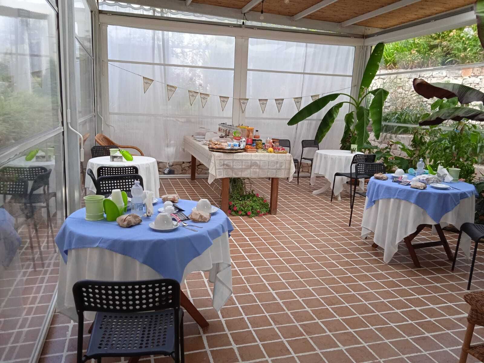 An outdoor patio with tiled flooring, tables with blue and white tablecloths, and chairs.