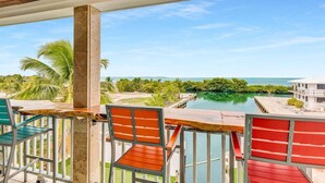 A balcony with a view of a calm body of water, palm trees, and a distant building.